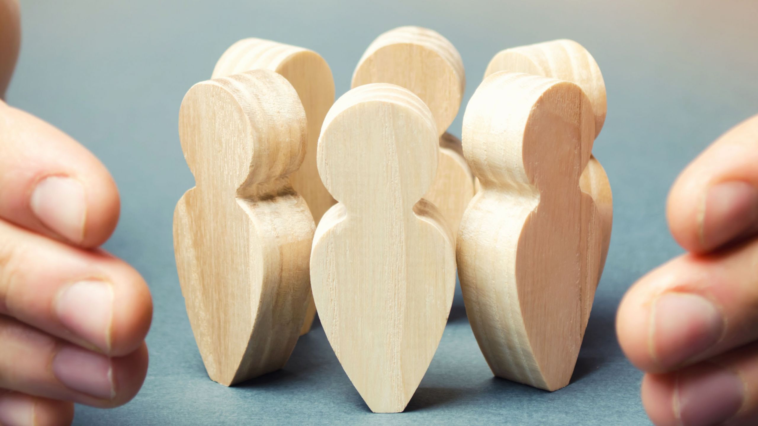 Zwei Hände schützen eine Gruppe von Menschen aus Holz.