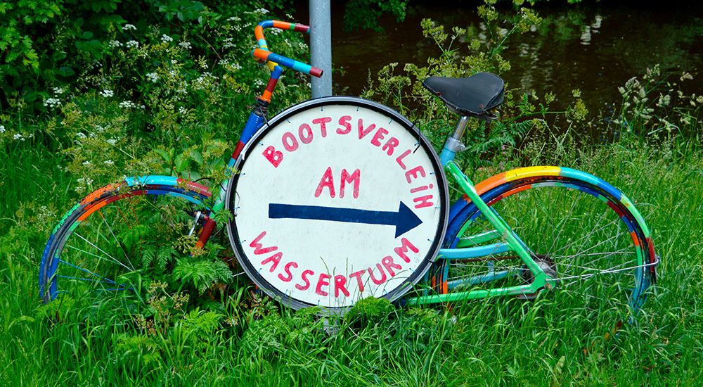 Buntes Fahrrad mit einem Wegweiser zum Bootsverleih.