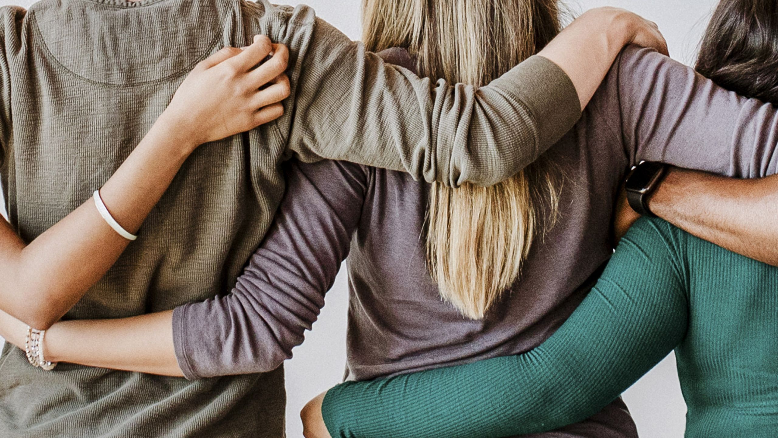 Mehrere Personen von hinten halten sich im Arm.