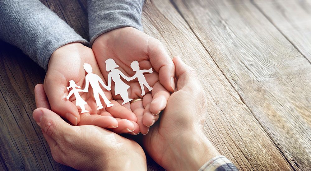 Hände mit Papiersilhouette einer Familie auf dem Tisch.