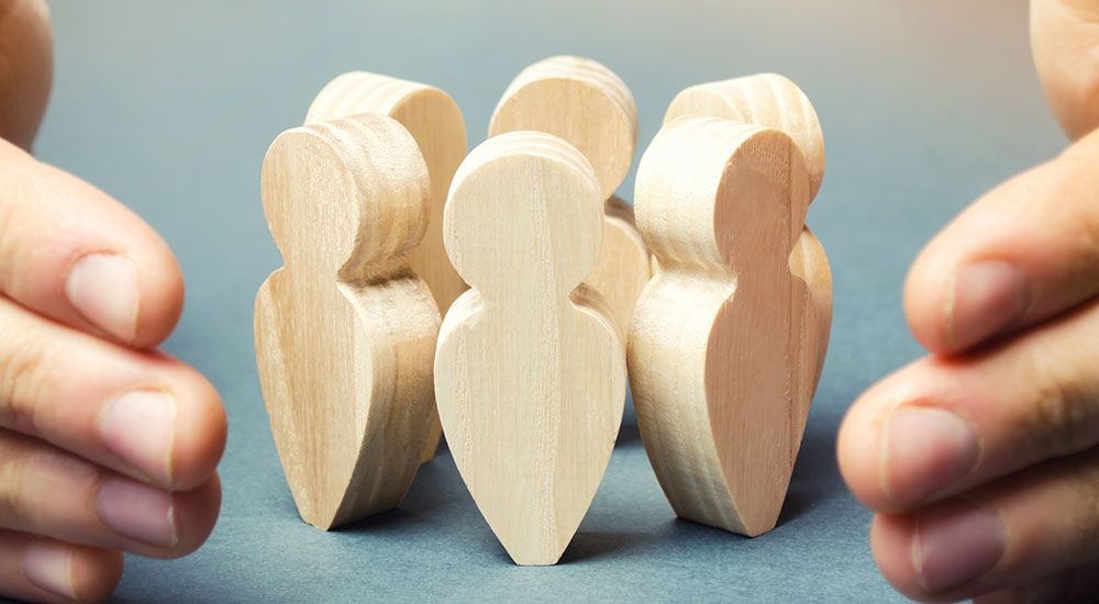 Zwei Hände schützen eine Gruppe von Menschen aus Holz.